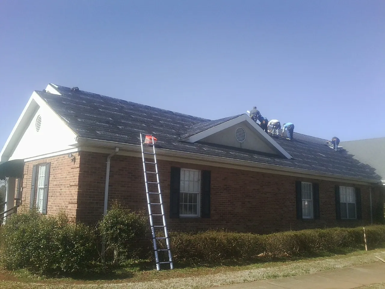 Crew tearing shingles off a brick ranch roof with a ladder set — Emergency Roof Repair work by our crew in Westerville