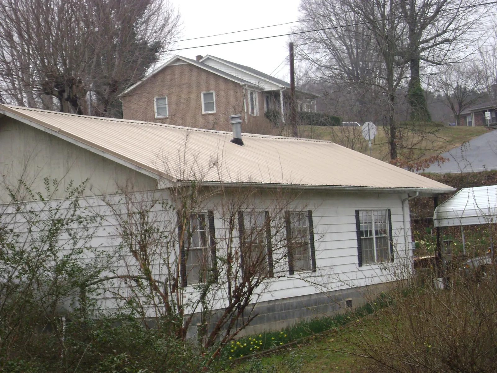 Tan metal roof on a white sided house set into a hillside — Commercial Roofing by Roofing Brothers in Westerville